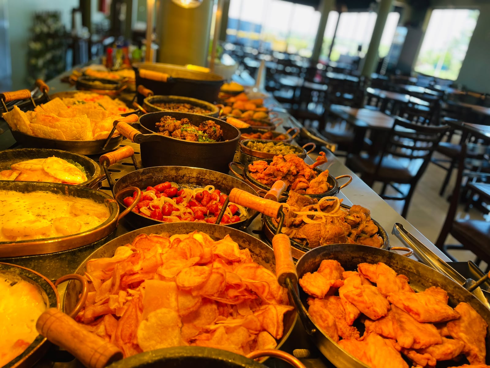 Buffet da Santa Brasa com pratos quentes, porções e saladas no balcão do restaurante