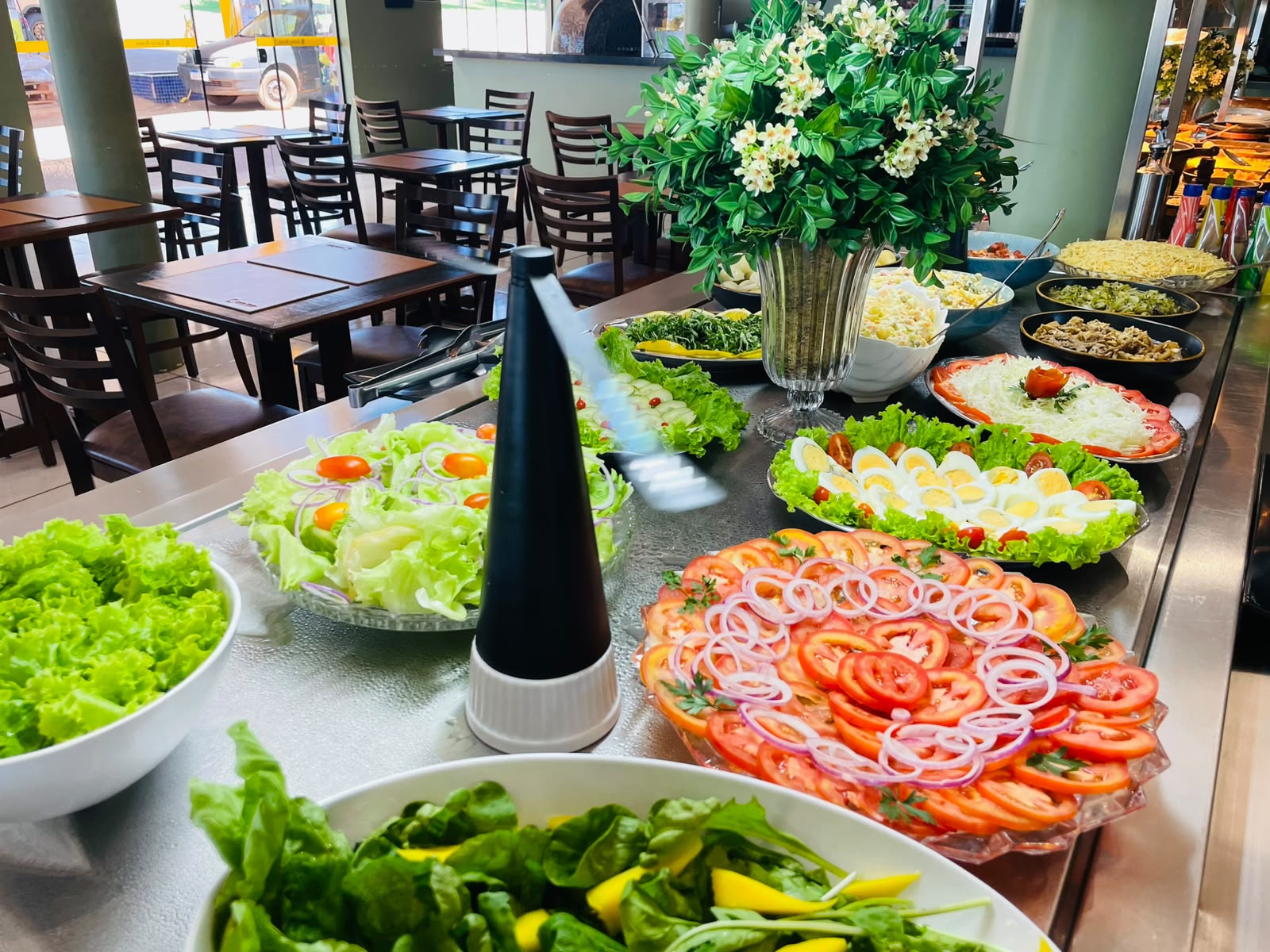 Ilha de saladas do Santa Brasa com tomate, ovos, alface e arranjo de flores